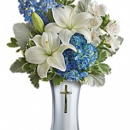 Arrangement of white lilies and blue hydrangea in a silver vase with a cross design