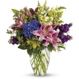 Bouquet of pink lilies, blue hydrangea, and purple flowers in a glass vase