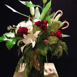 Holiday bouquet with red roses, white lilies, and candy cane accents in a vase