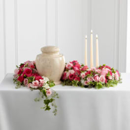 Pink rose arrangements around a beige urn with three taper candles