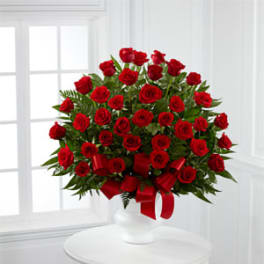 Red roses arranged in a white vase with a red ribbon