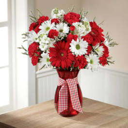 Red and white daisy bouquet in a red vase with a gingham ribbon
