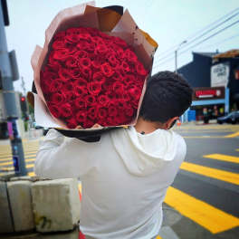 Large armful bouquet of tightly packed red roses wrapped in kraft paper, carried on a person's shoulder