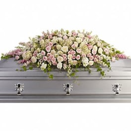 Long arrangement of soft pink and white flowers displayed on a silver casket
