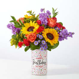 Mixed bouquet in a birthday vase with sunflowers, roses, and purple blooms