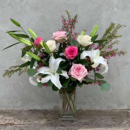 Pink and white roses with white lilies in a clear glass vase