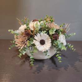 White floral arrangement in a round white bowl with trailing greenery