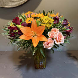 Mixed bouquet with orange lilies, pink roses, and yellow flowers in a glass vase