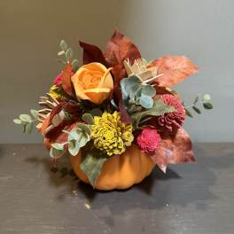 Autumn floral arrangement in a pumpkin container with orange, yellow, and pink blooms