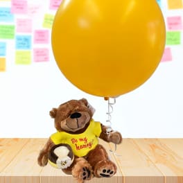 Teddy bear holding a large yellow balloon and a small honey pot