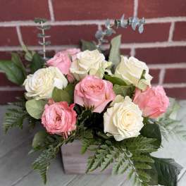Bouquet of pink and white roses with greenery in a square container