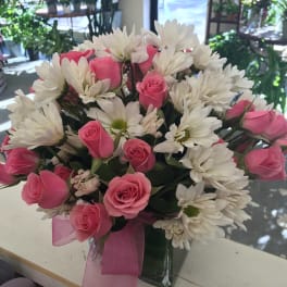 Pink roses and white daisies arranged in a clear vase with a pink ribbon.