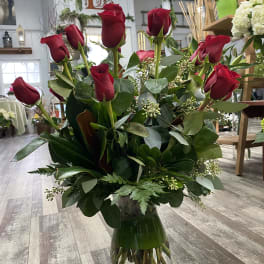 Red roses arranged in a clear glass vase with greenery