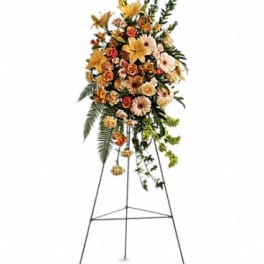 Standing spray of peach and orange lilies, roses, and gerbera daisies on an easel