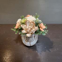 Small floral arrangement in a white ceramic pot with peach and cream blooms