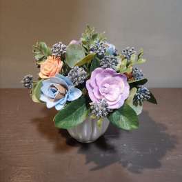 Small pastel floral arrangement in a silver vase with blue and lavender blooms