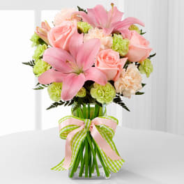 Pink lilies and roses arranged in a glass vase with a ribbon