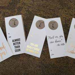 Five greeting card sleeves with gold and black text on a textured surface.