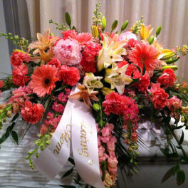 Large pink and coral floral spray with a white ribbon draped over a casket