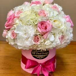 Pink and white roses arranged in a round hat box with a satin bow