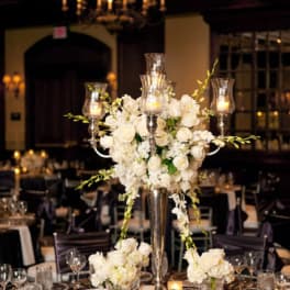 White floral centerpiece with candles in tall glass holders on a banquet table