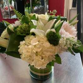 White floral arrangement in a glass vase with green accents