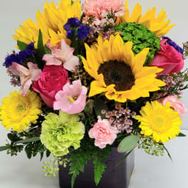 Bright mixed bouquet with sunflowers, pink roses, and carnations in a dark vase
