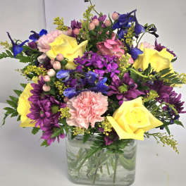 Bouquet of yellow roses, purple daisies, and pink carnations in a glass vase