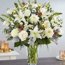 White lilies and roses in a clear glass vase with pinecones and ornaments