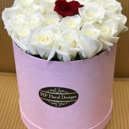 White roses with one red rose in a pink hatbox