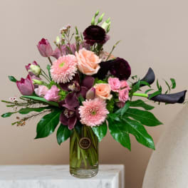 Mixed bouquet of pink, peach, and dark purple flowers in a glass vase