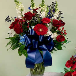 Red roses and white flowers in a glass vase with a blue ribbon