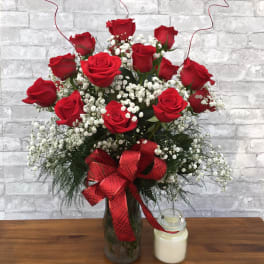 Red roses in a glass vase with baby's breath and a red ribbon