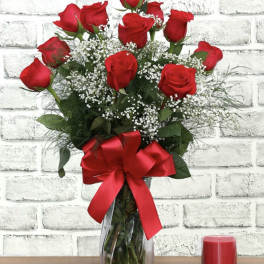 Red roses in a clear glass vase with a red ribbon and white filler flowers
