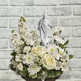 White floral arrangement with a small religious statue in a pedestal bowl