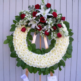 Large floral wreath with white daisies, red roses, and white lilies on an easel