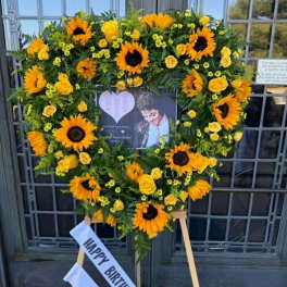 Heart-shaped sunflower and yellow rose standing wreath on an easel with a birthday ribbon