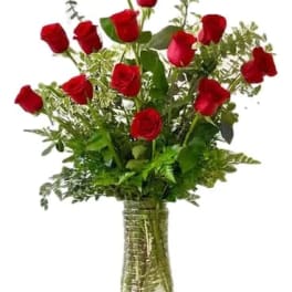 Red roses arranged in a clear glass vase with greenery