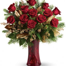 Arrangement of red roses with evergreen branches and gold accents in a red glass vase