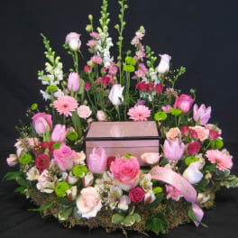 Pink and white floral arrangement surrounding a wooden box on a black background