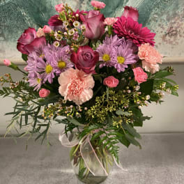Pink and lavender mixed bouquet in a clear glass vase with a ribbon.