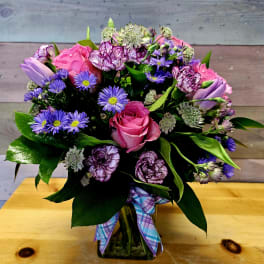 Bouquet of pink roses, purple daisies, and carnations in a glass vase