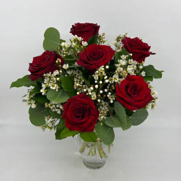 Small arrangement of red roses with tiny white filler blooms in a clear glass vase