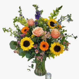Mixed bouquet with sunflowers, roses, and gerbera daisies in a glass vase
