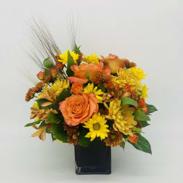 Compact arrangement of orange roses and yellow daisies in a black square vase