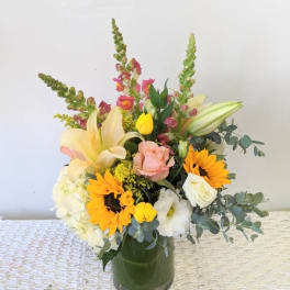 Mixed bouquet in a glass vase with sunflowers, lilies, roses, and tulips