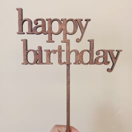Wooden "happy birthday" cake topper held in a hand