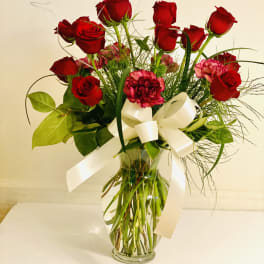 Red roses and pink carnations in a glass vase with a white ribbon