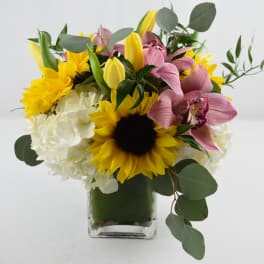 Bouquet of sunflowers, pink orchids, and white hydrangeas in a glass vase