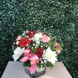 Bouquet of red, pink, and white flowers in a glass vase with a pink ribbon